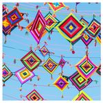 Many colorful, diamond-shaped pendants made of yarn are hung along a line with blue sky in the background.